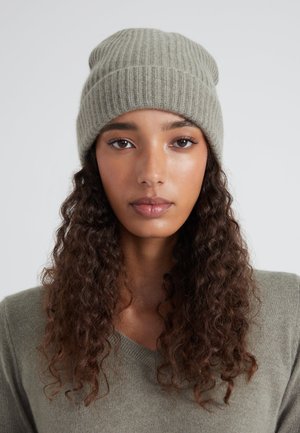 Bonnet tricoté gris-vert avec des côtes verticales. Texture douce et coupe décontractée. Design simple, sans motifs visibles ni éléments métalliques.