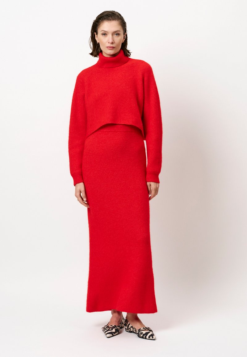 Rode gebreide twee-piece outfit met een cropped coltrui en een lange, aansluitende rok. Gelaagd stof en minimalistisch ontwerp.
