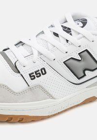 White sneaker with suede and leather materials, black accents, perforated details, model number 550, and a rubber outsole.