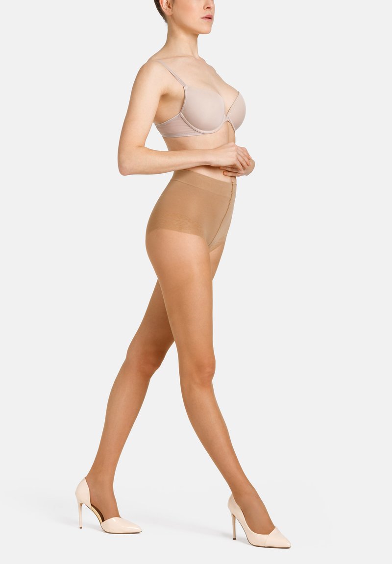 Beige sømløs bh med tynde stropper, parret med højtaljede nude-formende shorts. Model iført nude højhælede sko, der viser en glat tekstur.