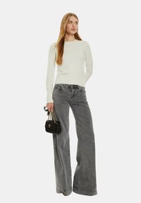 Maglione bianco a maglia con scollo rotondo abbinato a jeans grigi a vita alta e a gamba larga. Tiene una piccola borsa nera con hardware dorato.