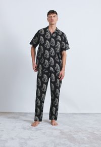 Schwarzes Pyjama-Set bestehend aus einem kurzärmeligen Shirt und langen Hosen, verziert mit einem detaillierten Tierdruck in Beigetönen. Weicher Stoff, lockere Passform.