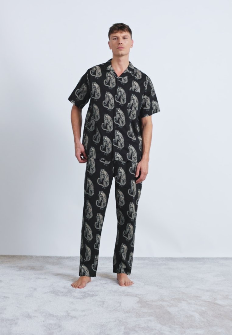 Ensemble de pyjama noir comprenant une chemise à manches courtes et un pantalon long, orné d'un imprimé animal détaillé dans des tons beiges. Tissu doux, coupe décontractée.