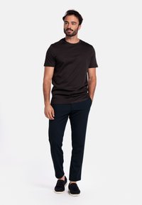 Zwarte crew-neck t-shirt, slim-fit marineblauwe broek en zwarte instappers. Gladde stof met een relaxte pasvorm, minimale details.