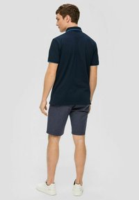 Granatowa koszulka polo z kontrastowym kołnierzykiem, w połączeniu z szarymi szortami. Model nosi białe trampki. Prosty i casualowy design.