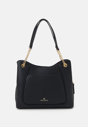 Schwarze Handtasche mit strukturiertem Finish, ausgestattet mit Kettenakzenten an den Griffen, einer auffälligen Fronttasche und einer goldfarbigen Markenprägung am Boden.