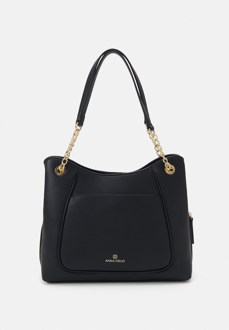Borsa nera con finitura testurizzata, presenta accentuazioni in catena sulle maniglie, una tasca frontale prominente e un marchio dorato nella parte inferiore.