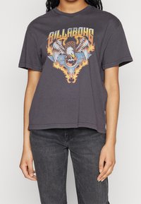 Camiseta de algodón gris oscuro con un gráfico central de un águila con alas, llamas y texto. Mangas cortas y corte relajado.