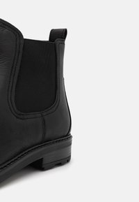 Bottine en cuir noir avec panneau latéral élastique, languette à l'arrière et talon bas empilé.