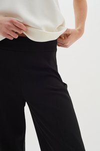 Svarta vida byxor i ett mjukt, flödande tyg. Har hög midja och fickor, kombineras med en ljus krämfärgad topp.