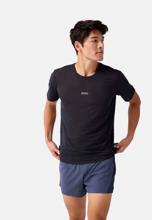 Zwarte sportieve t-shirt met een gewoven ontwerp, met een ronde hals en een klein logo op de borst. Draagt bij een marineblauwe broek.