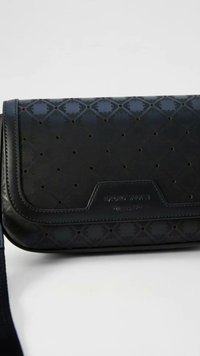 Μαύρη ορθογώνια τσάντα crossbody με γεωμετρικό διάτρητο σχέδιο και ανάγλυφο όνομα μάρκας στο μπροστινό καπάκι, σε λευκό φόντο.