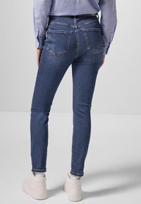 Jeans ajustados en denim azul oscuro, con un diseño clásico de cinco bolsillos, detalles de costura sutiles y una cintura de altura media.