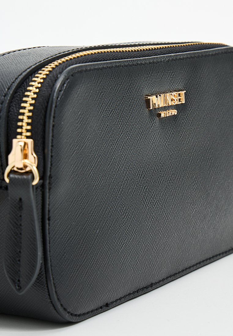 Czarna kosmetyczka wykonana z teksturowanego materiału syntetycznego, z złotym zamkiem i detalami logo, o prostokątnym kształcie i gładkim wykończeniu.