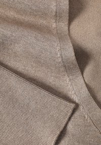 Pull beige avec un tricot doux et texturé. Gros plan montrant des coutures lisses et un col côtelé, avec un pli à l'ourlet.