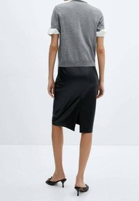 Grauer Kurzarm-Pullover mit weißen Akzenten, kombiniert mit einem schwarzen Satin-Midirock mit einem Rückenschlitz, getragen mit schwarzen Absatzsandalen.