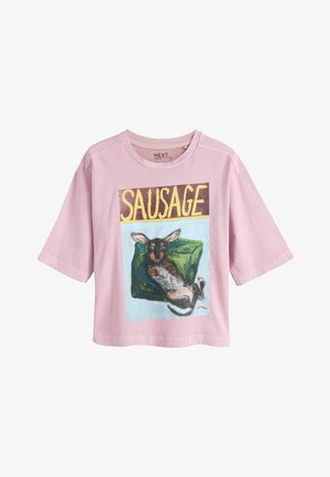 Light pink short-sleeve shirt with a graphic of a relaxed dog lying on a green cushion and the word "SAUSAGE" in large yellow letters above.