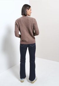 Brun, texturerad tröja med ribbad nederkant, parat med mörka, utsvängda jeans. Outfiten fulländas med ljusa sneakers.