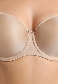 Reggiseno imbottito beige con tessuto liscio, supporto con ferretto e chiusura centrale. Presenta un design senza cuciture e una cucitura decorativa ai bordi.