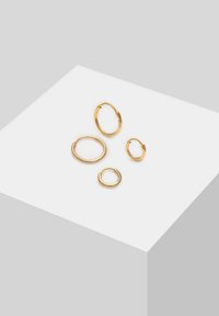 Cinco pendientes de aro de metal dorado en tamaños variados, con superficies lisas y formas redondas, acabado pulido y cierres simples.