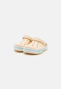Beżowe klapki z formowanego materiału z otworami wentylacyjnymi, tealowy pasek u podstawy oraz wytłoczone logo "Crocs" z boku. Lekka i elastyczna konstrukcja.