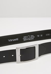 Ceinture en cuir noir avec une boucle rectangulaire en argent, comportant des marquages de taille et le texte "Fabriqué en Allemagne" sur le dessous.