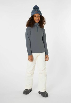 Grijze lange mouwen top met half-rits ontwerp, witte geïsoleerde broek en zwarte sneeuwlaarzen. Gebreide blauwe muts met pompon accent.