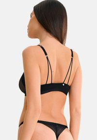 Ensemble de lingerie noire comprenant un soutien-gorge transparent à pois avec des bretelles ajustables et un string assorti, mettant en avant une texture lisse et un design minimaliste.