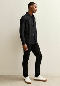 Zwarte overhemd met knopen en een gestructureerde afwerking, gecombineerd met zwarte broek en witte sneakers. Eenvoudig ontwerp met een comfortabele pasvorm.