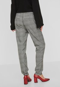 Pantalon à carreaux gris avec taille élastique et poches latérales, associé à des chaussures à talons carrés en cuir verni rouge.