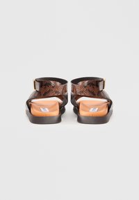 Sandalias de reptil en relieve de color marrón con un talón abierto, correa ajustable en el tobillo, plantilla naranja y suela texturizada marrón.