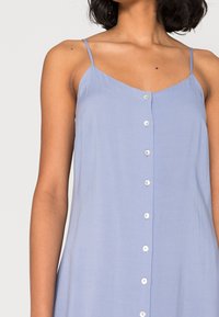 Hellblaues ärmelloses Kleid mit V-Ausschnitt und sechs Frontknöpfen in einer geraden Reihe. Glatte Stoffstruktur und verstellbare dünne Träger.