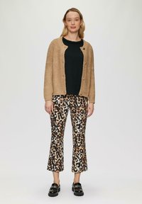 Beige gebreide cardigan over een zwarte textuurtop, gecombineerd met flared broeken met luipaardprint. Het model draagt zwarte instappers.