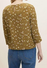 Braune Bluse mit floralen Mustern und Dreiviertelärmeln, mit einem Schlüsselrücken, strukturiertem Stoff und verstreuten weißen, rosa und grünen Motiven.