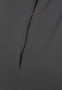 Tecido cinza escuro com uma textura suave, apresentando uma fenda e um detalhe de botão redondo em tom dourado. O tecido é elástico e leve.