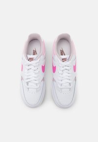 Bílé tenisky s růžovými akcenty. Hladký kožený svršek, perforovaná špička, ploché bílé tkaničky a růžové logo swoosh na stranách. Zaoblený tvar špičky.