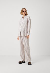 Ensemble de pyjama léger à rayures pastel composé d'une chemise à boutons et de pantalons larges, associé à des sandales à talons ouverts noires.