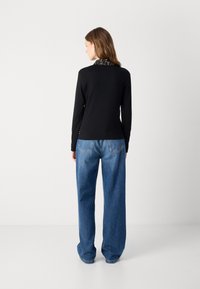 Zwarte lange mouw top met een gemusterde kraag, gecombineerd met ruime blauwe denim jeans. De jeans hebben een standaard snit en achterzakken.