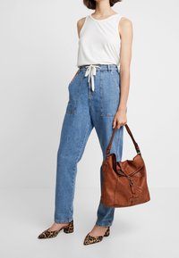 Top bianco senza maniche, pantaloni in denim blu a vita alta, tacchi con stampa leopardata e una borsa in pelle marrone con un design morbido e accessori metallici.