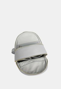 Zaino grigio dalla forma arrotondata, dotato di chiusura con zip, una morbida fodera interna e una tasca frontale. Accentuato da accessori in oro.