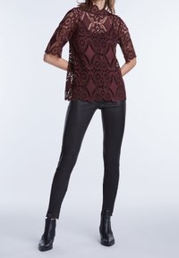 Burgunderfarvet bluse i blonder med høj hals og bølgekant, der har detaljerede blomster mønstre. Kombineret med sorte læderbukser og ankelstøvler.