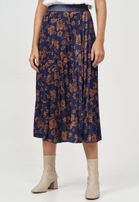 Marinblå plisserad kjol med brunt blommönster, elastisk midja med metallisk detalj, längd till mitten av vaden, kombinerad med beige ankelboots.