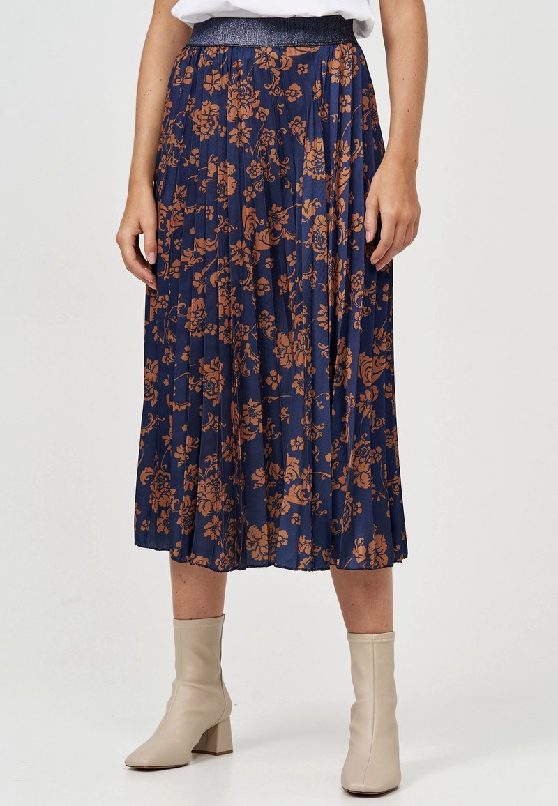 Marinblå plisserad kjol med brunt blommönster, elastisk midja med metallisk detalj, längd till mitten av vaden, kombinerad med beige ankelboots.