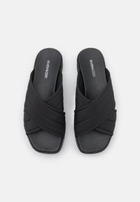 Sandali neri con fasce incrociate in tessuto imbottito, punta squadrata e suola piatta. Presentano una superficie liscia e un design minimalista.