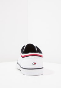 Baskets blanches avec un corps en cuir texturé, un col élastique noir, et des bandes rouges et marine. Présentent un petit logo près du talon.