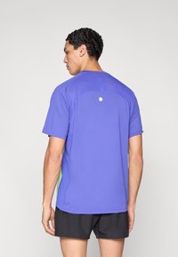 Μωβ αθλητικό πουκάμισο με υφή, κοντά μανίκια και λευκή κυκλική λεπτομέρεια στην πλάτη, συνδυασμένο με μαύρο σορτς.