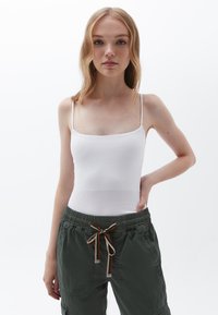 Witte geribde tanktop met dunne schouderbandjes, gecombineerd met olijfgroene cargobroek met trekkoord en zijzakken, gemaakt van een textuurstof.