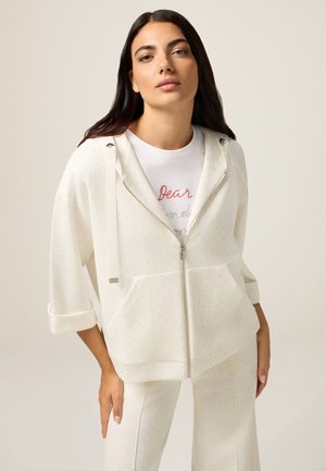 White hoodie with a zip front, dotted pattern, and drawstring hood. Paired with matching white pants, featuring a relaxed fit.