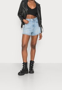 Chaqueta de cuero negro estilo biker sobre un top corto negro acanalado, combinada con pantalones cortos de mezclilla azul claro y botas negras hasta la rodilla con hebillas.