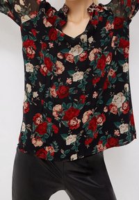 Blusa nera floreale caratterizzata da un design a motivi con rose rosse e crema, maniche trasparenti e scollatura con bottoni. Realizzata in tessuto leggero.